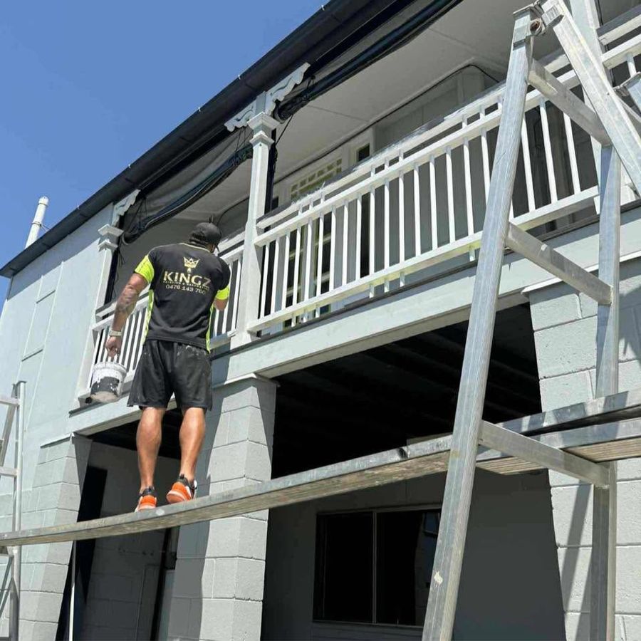 A Kingz painter on scaffold cutting in the underside of a two-storey balcony.