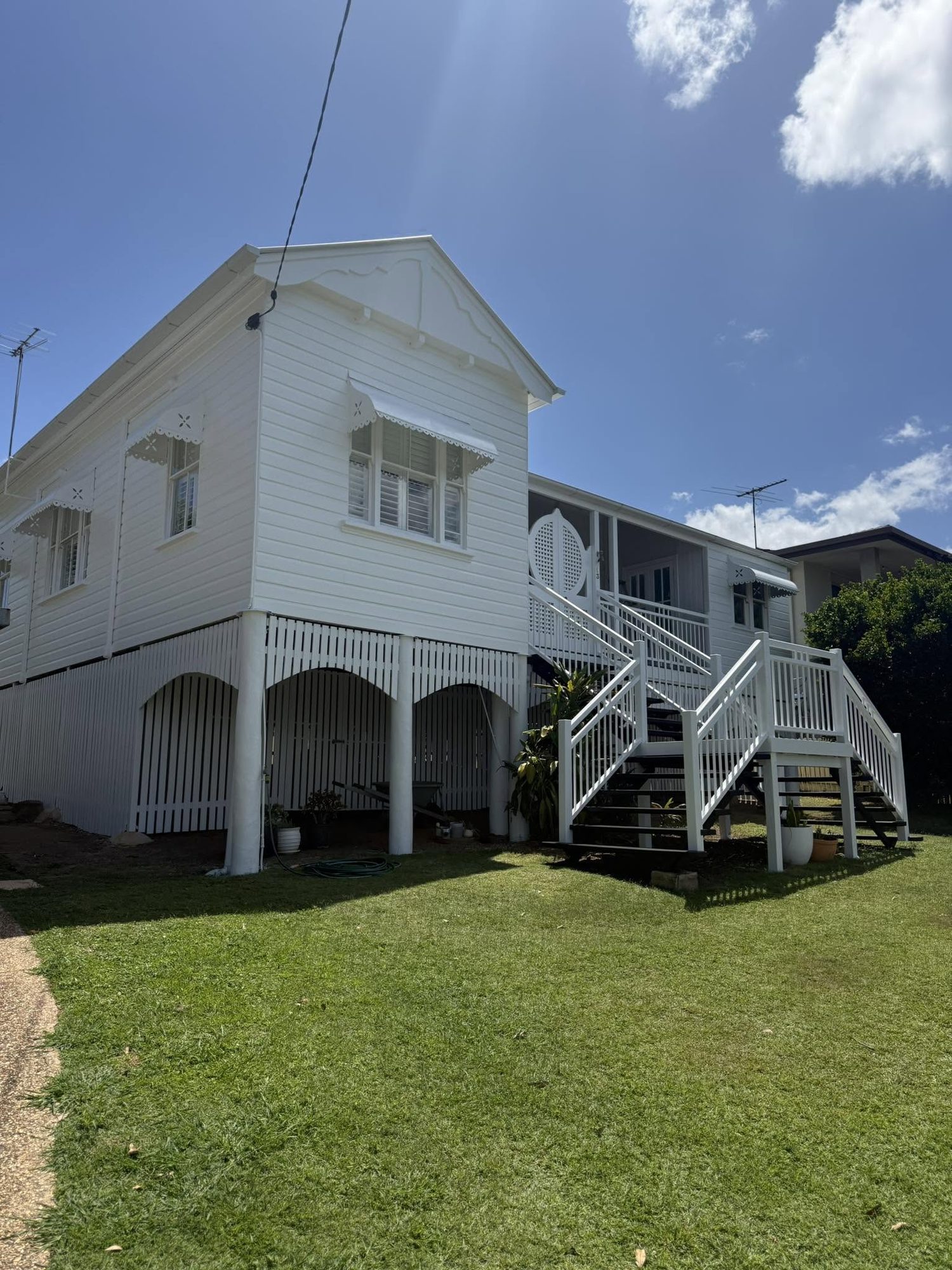 A freshly repainted white Queenslander in Ipswich, showing restored fretwork, gable detail and new stairs.
