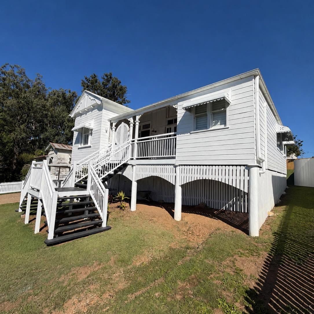Side elevation of a restored white Queenslander with new balustrades, lattice and dark stair treads.
